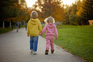 Cute blond toddler children boy and girl,walking in autumn park on sunset, enjoying the beautiful nature