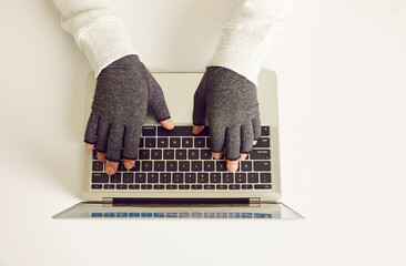 Patient with rheumatoid arthritis working on computer wearing pair of warm comfortable fingerless...