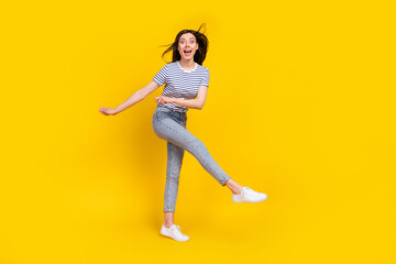 Full size photo of funky satisfied overjoyed lady slim figure raise arm palm leg good mood empty space isolated on yellow color background