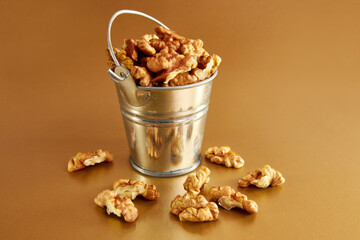 A small metal bucket filled with walnuts on an orange background. Concept of healthy eating.