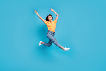 Fototapeta na wymiar Full length photo of shiny excited lady wear yellow t-shirt jumping high hurrying rising arms isolated blue color background