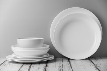 a set of white ceramic tableware on a light background. Various types of white plates, bowls and platters, cups, saucers, milkmen. Simple white tableware for use at home or in a cafe.
