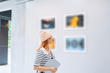 Woman visiting art gallery her looking pictures on wall watching photo frame painting at artwork...