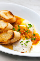 white fish with tomato sauce and roasted baguette slices