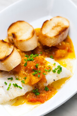 white fish with tomato sauce and roasted baguette slices