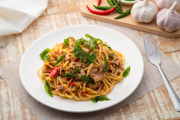 Stir fried Spaghetti with Canned tuna fish and crispy basil leaves in white plate,Spicy pasta Pad Kra Pao.Thai fusion food