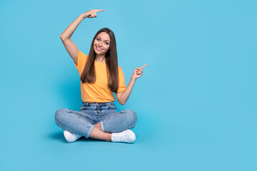 Photo of sweet charming lady wear yellow t-shirt sitting legs crossed pointing two fingers empty...