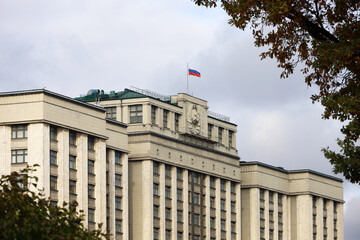Fototapeta na wymiar Parliament building with Russian flag in Moscow. The State Duma facade, view through the branches of autumn trees