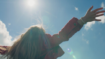 Young girl moves long hair, enjoying flows of warm wind, beautiful sun rays swimming at clouds,...