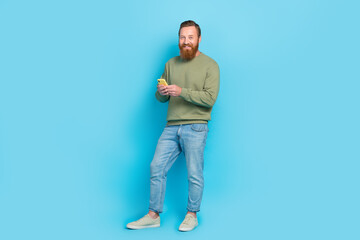 Fototapeta premium Full length photo of nice young man hold smartphone typing reading news dressed stylish khaki look isolated on aquamarine color background