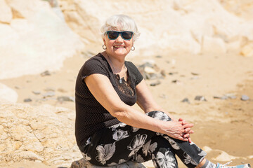 Old woman in black clothes sitting on a rock near the sea and having fun.