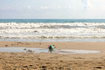 Beach in Valencia, Spain, Port Saplaya, where you can see a plastic bucket in the sand, and some waves in the Mediterranean sea