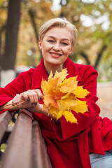 Portrait of a beautiful middle-aged woman in a red coat, autumn park