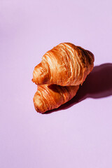 Two fresh and soft croissants on a purple background with room for text. Stylish baking and bakery concept