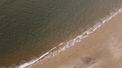 Aerial view looking straight down onto a sandy beach with waves rolling in. © ReayWorld