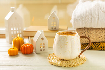 Autumn composition, a cup of hot coffee, a decorative little house, pumpkin candles, books and a warm sweater on a wooden table. Seasonal morning hot coffee. Cozy interior decor