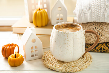 Autumn composition, a cup of hot coffee, a decorative little house, pumpkin candles, books and a warm sweater on a wooden table. Seasonal morning hot coffee. Cozy interior decor