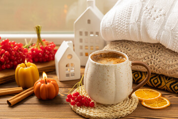 Autumn composition, a cup of hot coffee, a decorative little house, pumpkin candles, books and a warm sweater on a wooden table. Seasonal morning hot coffee. Cozy interior decor