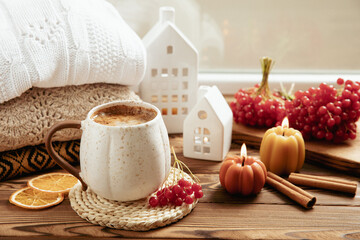 Autumn composition, a cup of hot coffee, a decorative little house, pumpkin candles, books and a warm sweater on a wooden table. Seasonal morning hot coffee. Cozy interior decor