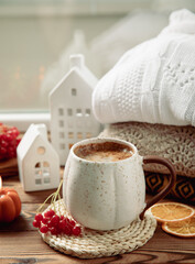 Autumn composition, a cup of hot coffee, a decorative little house, pumpkin candles, books and a warm sweater on a wooden table. Seasonal morning hot coffee. Cozy interior decor