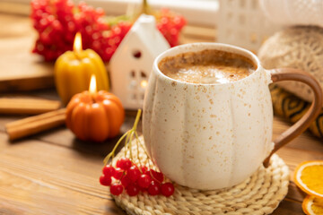 Autumn composition, a cup of hot coffee, a decorative little house, pumpkin candles, books and a warm sweater on a wooden table. Seasonal morning hot coffee. Cozy interior decor