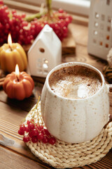 Autumn composition, a cup of hot coffee, a decorative little house, pumpkin candles, books and a warm sweater on a wooden table. Seasonal morning hot coffee. Cozy interior decor