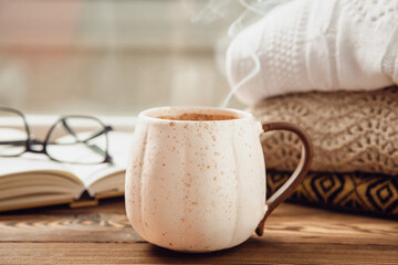Autumn composition, a cup of hot coffee, a decorative little house, pumpkin candles, books and a warm sweater on a wooden table. Seasonal morning hot coffee. Cozy interior decor