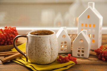 Autumn composition, a cup of hot coffee, a decorative little house, pumpkin candles, books and a warm sweater on a wooden table. Seasonal morning hot coffee. Cozy interior decor