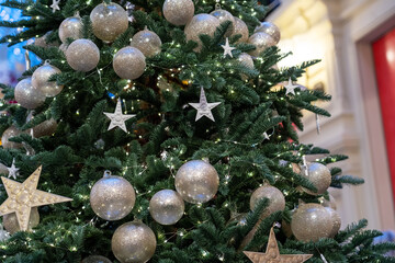 Close up of christmas glitter decorations balls and stars hanging on illuminated tree indoor of a shopping mall or department store