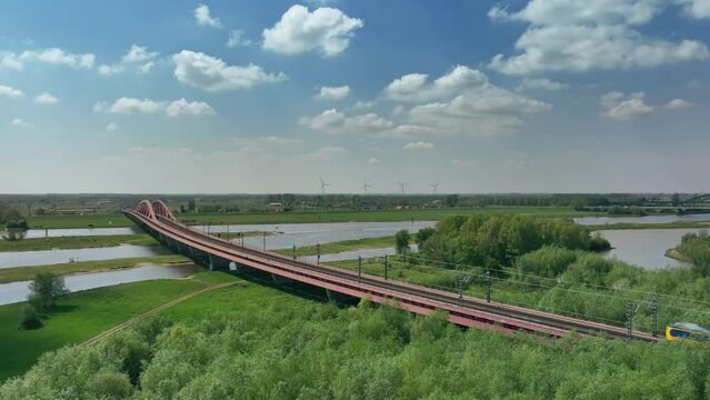 Train driving over the Hanzeboog train bridge over the river IJssel near the city of Zwolle in Overijssel during a springtime day. Aerial drone point of view.