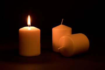 power outages concept, three candles, one with flame and two reserve, on the desk, dark background