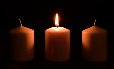 power outages concept, three candles, one with flame and two reserve, on the desk, dark background