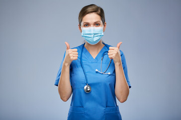 Nurse woman or doctor in blue medical mask showing thumbs up. Isolated female portrait.
