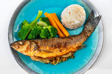 Fried trout with vegetable garnish and rice on blue plate.