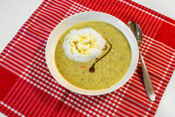 Broccoli soup with sesame seed, black cumin oil and cream on red checkered table-cloth.