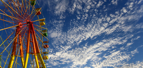 Attraction (carousel) ferris wheel on the background of the cloudy sky