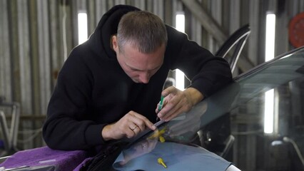 Professional windshield repairman fills a crack in the glass with a special polymer through a syringe. Elimination of cracks and chips on windshields