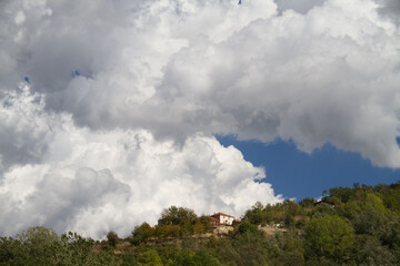 Cumulus clouds, large white clouds, above a village on a wooded hill in Tuscany, Italy