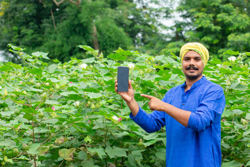 Indian farmer showing smartphone screen at green agriculture field