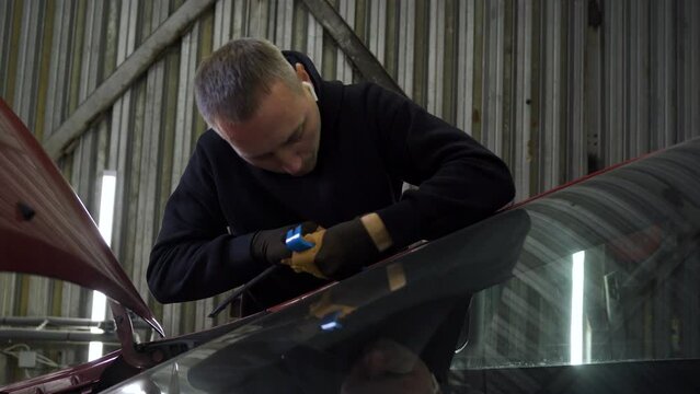 Professional windshield repairman fills a crack in the glass with a special polymer through a syringe. Elimination of cracks and chips on windshields