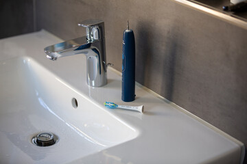 Elektrische Zahnbürste mit Aufsatz auf dem Waschbecken neben dem Wasserhahn