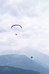 Two paragliders flying over mountains on a cloudy day at french alps. 