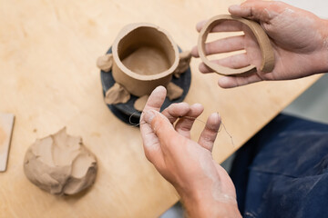 Top view of man holding fishing line and clay in pottery studio.