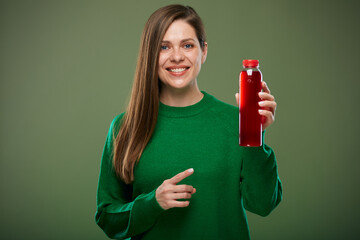 Smiling woman holding bottle with red juice and pointing finger. Isolated advertising portrait on...