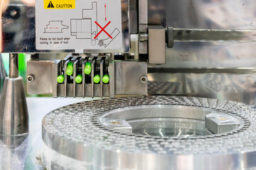 close up medicine green capsule at feeding fork of automatic capsule filling machine during manufacturing process in industrial