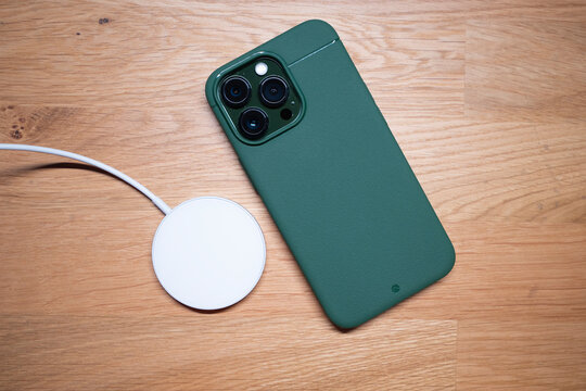 Kuala Lumpur - Malaysia Oct 8 2022 : Close up of the new iPhone 13 Pro Alpine Green new color with premium case by Caudabe Sheath on wooden background with a magsafe fast charging