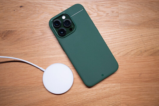 Kuala Lumpur - Malaysia Oct 8 2022 : Close up of the new iPhone 13 Pro Alpine Green new color with premium case by Caudabe Sheath on wooden background with a magsafe fast charging