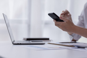 Fototapeta premium Image of smiling attractive and charming asian woman using mobile phone while working on laptop in modern office