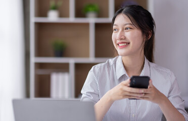 Image of smiling attractive and charming asian woman using mobile phone while working on laptop in modern office