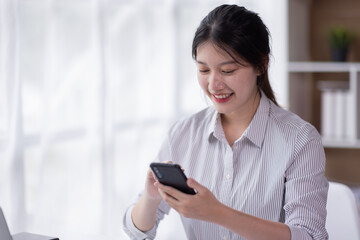 Image of smiling attractive and charming asian woman using mobile phone while working on laptop in modern office